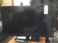 Front view of Insignia 32" LED TV with stand and remote on a wooden surface, showing the entire screen and base stand.