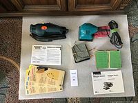 Both electric palm sanders, one Black & Decker 3 in 1 Total Task Sander and one Makita Finishing Sander, with instruction manuals and sanding sheets laid out on a white surface.