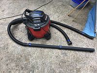 Full view of the Craftsman shop vacuum, showing red body, black top handle, hose, and wand attachment on concrete floor.