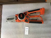 Alligator Lopper saw tool full view laid flat on white mat showing orange and black handles and saw blade.