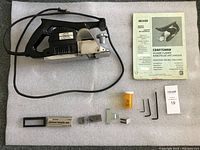 Front view of Craftsman power planer with power cord, manual, planer blade set, multiple Allen wrenches, and orange container on a white surface.