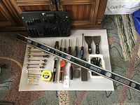 Photo showing the full layout of assorted hand tools including wrenches, screwdrivers, scrapers, oil stones and hex wrenches with a 4' Mastercraft level laid diagonally.