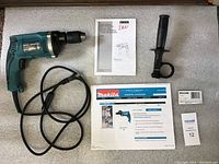 Makita HP1631K hammer drill with cord, side handle, manual, documentation, and tool case, all displayed on foam.