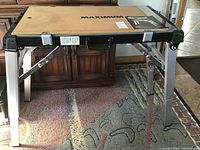 Portable multi-purpose work bench fully set up with foldable aluminum legs and wooden top with Maximum branding.