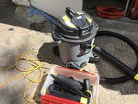 Overall view of the Maximum shop vacuum with accessories in plastic bin on concrete floor.