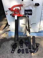 Full view of Toro Ultra Blower Vac with two white leaf bags and multiple black plastic parts laid out in front on concrete surface.