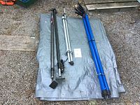 Overview of all poles laid on a gray tarp outside showing two black cargo keepers, two silver tent poles, and three blue ratchet poles tied together.