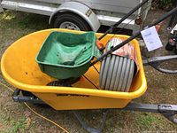 Yellow True Temper wheelbarrow with fertilizer spreader and garden hose inside