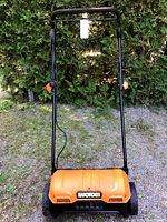 Front view of the orange and black Worx electric corded dethatcher with foldable handle in a garden setting.