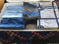 Eight towels shown folded in a box: three larger beach size towels including a white towel with navy ropes pattern, and five assorted bath towels in shades of blue and striped pattern.