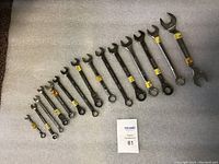 Photo of 15 combination wrenches arranged in size order from largest to smallest on a grey fabric surface with a MaxSold lot card visible.