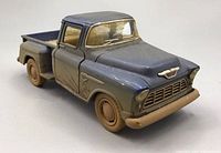 Front and side view of the 1955 Chevy Stepside Kinsmart diecast truck showing blue paint and muddy dirt effect on tires and bumper.