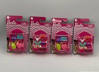 Four unopened Barbie accessory packs in original packaging, each including a miniature handbag, wallet, drink cup and a pineapple-shaped accessory.