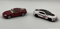 Front and side view of the red Jaguar XK Coupe and white Chevrolet Camaro diecast models showing overall condition and details.