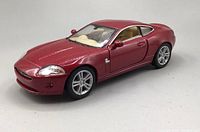 Front angled view of red Jaguar XK Coupe model car showing front grille, headlight detail, and side mirror.