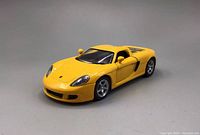 Front and side view of yellow Kinsmart Porsche Carrera GT model car showing intact body paint, clear windows, and detailed headlights.