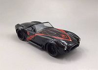 Front right angle view of black Shelby Cobra 1965 diecast model with red spider web and spider designs on hood and sides.