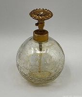 Photo of a round crackled glass perfume bottle with a gold-colored decorative pump dispenser on top.
