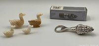 Four vintage duck figures and a silver tone Elegance brand grape cluster bottle stopper with box shown together on white surface.