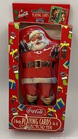 Front view of the vintage Coca-Cola Santa tin packaging showing Santa holding bottles and labeling indicating two decks of playing cards inside