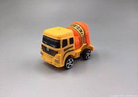 Yellow and orange toy cement mixer truck viewed from the side showing the cab, mixer drum and wheels.