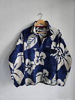 Men's Patagonia Synchilla Snap-T fleece pullover hanging on a wooden hanger, showing full front with blue and cream floral pattern.