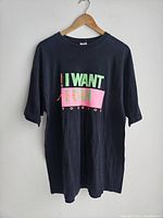 Full front view of black Adidas T-shirt on wooden hanger showing graphic text and overall condition.