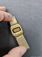 Top view of vintage Bulova digital LCD watch with gold tone bezel and textured band shown in hand for scale.