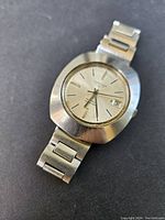 Front view of cushion-shaped stainless steel case, silver dial, date window at 3 o’clock