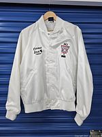 Front view of white satin jacket with embroidery that includes 'tara Inn Ventura' and logo for NCI Hard Ice Live Blue.