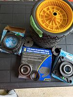 Photo showing two yellow plastic wheels with black rubber tires, two mounted bearing housings, a sealed bearing, and packaged #35 roller chain.