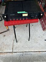 Front angled view of the Genexxa MPA-101 mono PA amplifier showing front panel controls, level meter, rack mount ears, and rust spots on the black metal casing.