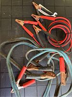 Two sets of jumper cables, one with red and black clamp insulation and cables, the other older with blue cables and rusty clamps