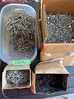 Top view of assorted metal nails in plastic container and cardboard boxes.
