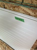 White paneling sheets stacked against a chipboard wall, showing beadboard groove style and 'LOT #11' label.
