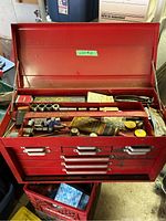 Photo of the open red metal toolbox with tools in the top compartment including sockets and caulking gun