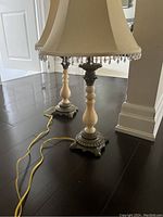 Full view of two vintage table lamps with cream-coloured marble bases, ornate metal feet, and beige fabric bell-shaped shades with crystal bead accents.