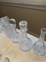 Photo showing four crystal decanters with various stoppers and patterns from the side, one missing its stopper.