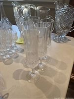 Photo showing 5 crystal champagne flutes, clear with vertical patterns and decorative stems, arranged in a row on a light surface.