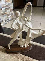 Side view of the male and female dancing couple sculpture showing detailed carving, clothing folds, and base.