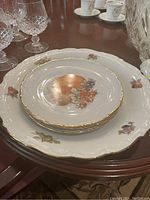 Stack of smaller porcelain plates with floral and fruit motifs and gold trim on a large plate with matching design.