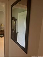 Mirror hanging on a wall reflecting a door, showing the side view of the brown frame and the clear mirror surface.
