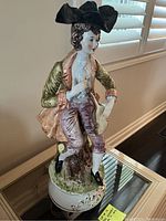 Full view of Capodimonte porcelain boy statue seated on a round base, showing detailed coloring and clothing.