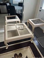 Overview of the cream colored coffee table and two matching end tables with glass inset tops, arranged on a floor near kitchen and door.