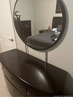 Front and side view of the espresso stained dresser with smooth, rounded top and visible metal knobs on drawers and cupboards, mirror visible above.