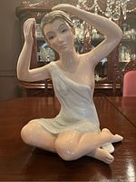 Front view of the porcelain statue showing the seated woman with hands raised to her head.