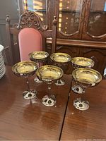 Six gold plated chalice style cups displayed on a wooden dining table, showing overall condition and style.