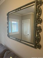 Front view of the rectangular green wrought iron framed mirror mounted on the wall above a couch, showing the grapevine decorative elements on the frame.