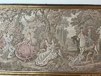 Framed large Victorian needlepoint textile picture on wall, showing detailed outdoor scene with figures and animals.