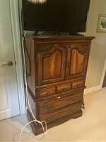 Full front view of the oak dresser showing the upper cupboard with doors, three middle drawers, and two lower drawers. The dresser has decorative carved edges and metal hardware.